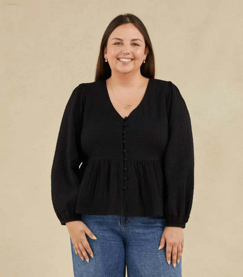 a woman wearing a black top and blue jeans is smiling