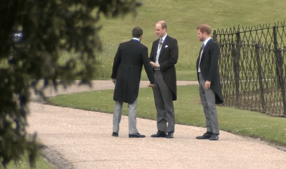 three men in suits are standing on a gravel path talking to each other