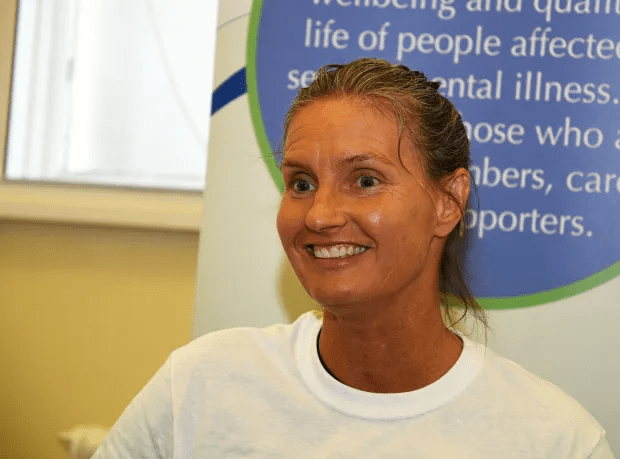 a woman smiles in front of a sign that says life of people affected by mental illness