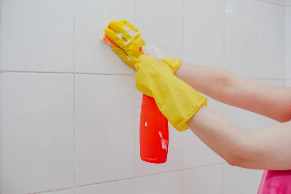 a woman wearing yellow gloves is cleaning a wall with a spray bottle