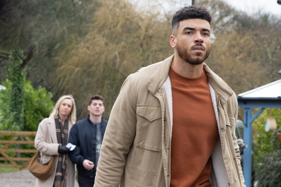 a man in a tan jacket stands in front of a group of people