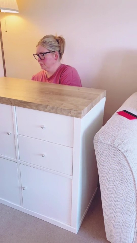 a woman wearing glasses sits behind a white dresser