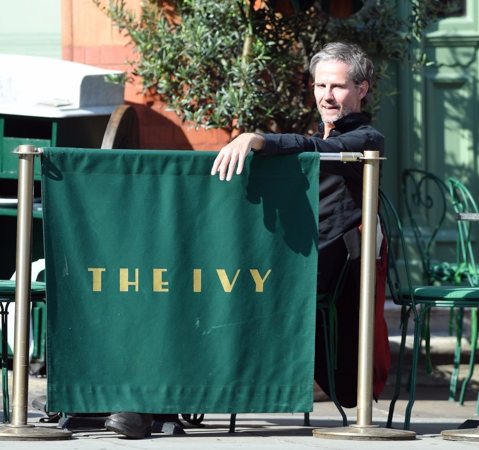 a man leans against a green sign that says the ivy