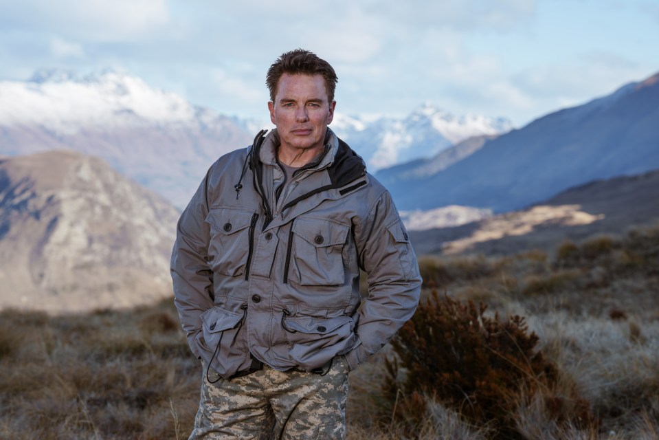 a man in a camouflage jacket stands in front of a mountain