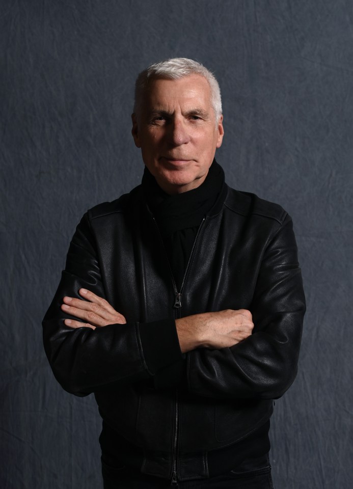 a man in a black leather jacket stands with his arms crossed