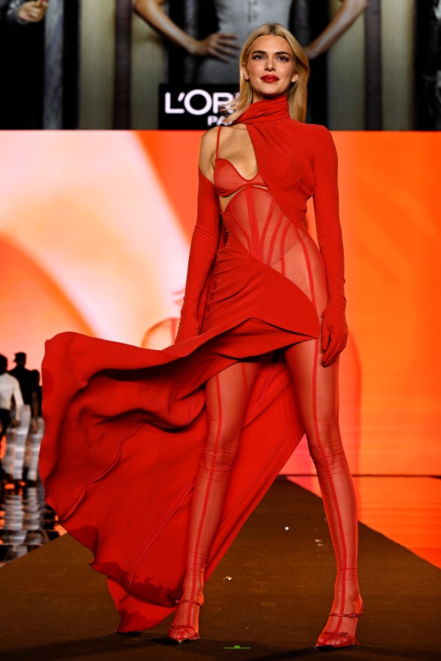 a woman in a red dress is walking down a runway in front of a screen that says l' oreal