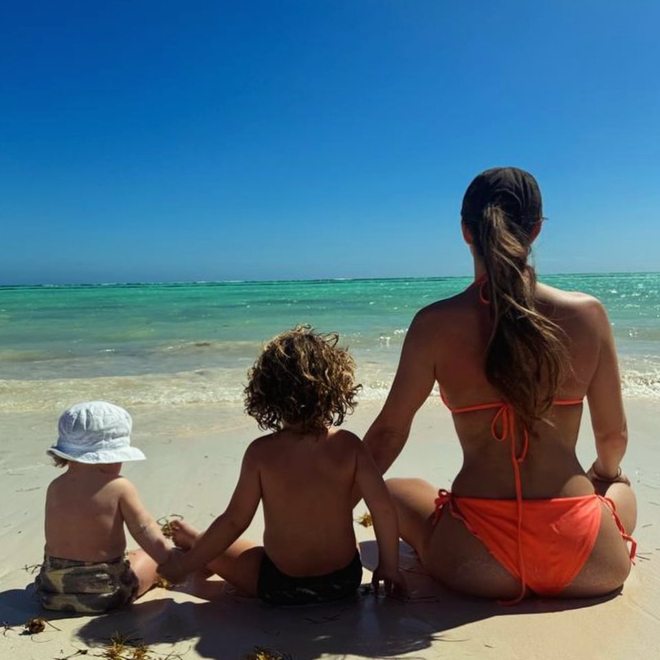 a woman in an orange bikini sits on the beach with two children