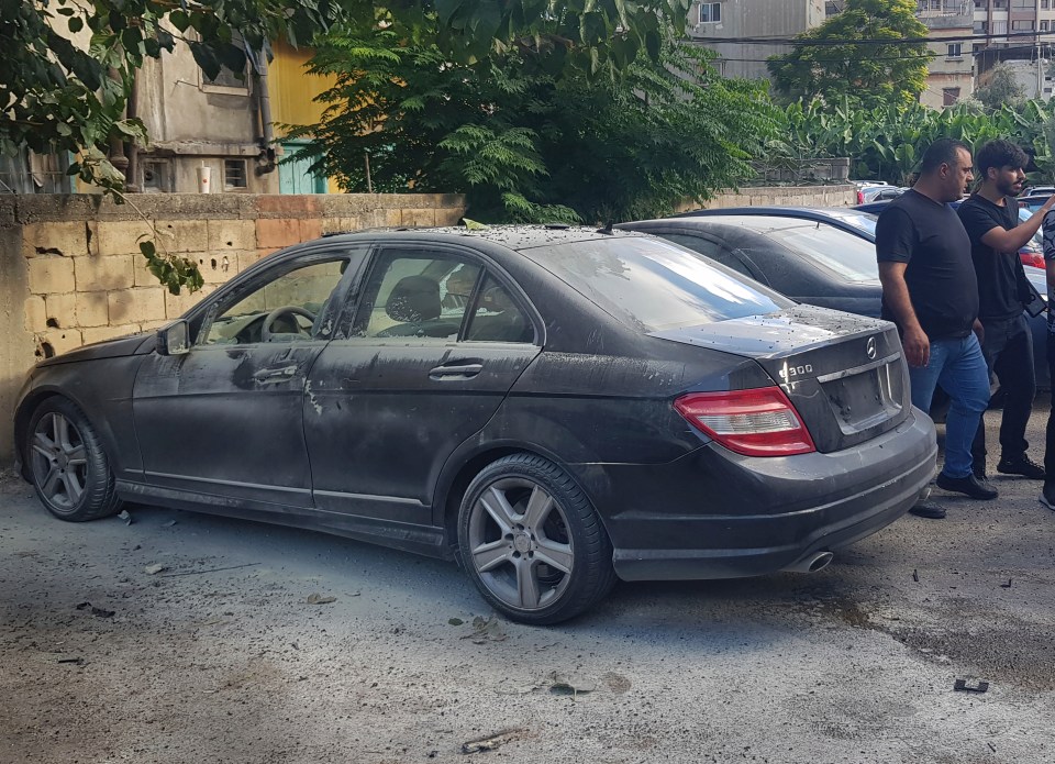 Lebanese security officers stand next of a partly damaged car after a walkie-talkie exploded inside it