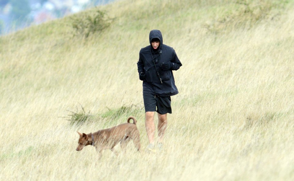 a man in a black jacket walking a dog in a field