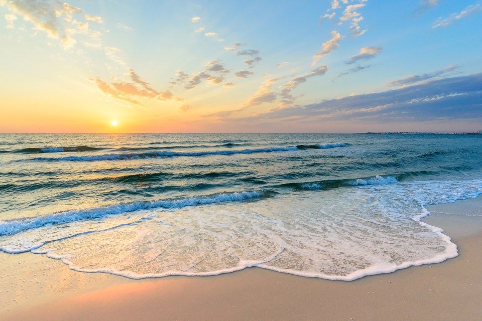 the sun is setting over the ocean with waves crashing on the beach