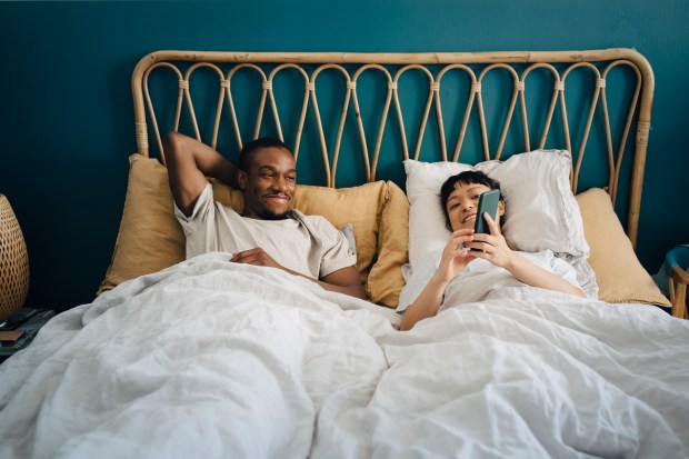 a man and a woman are laying in bed looking at their phones