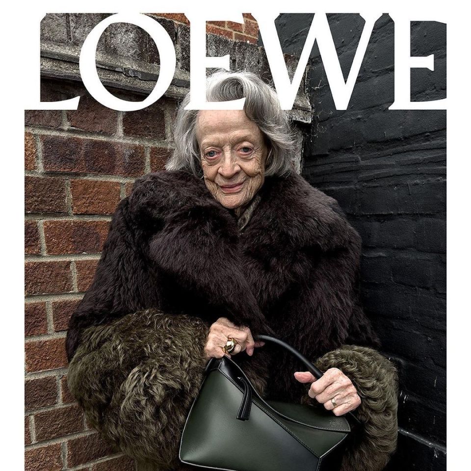 a woman in a fur coat holds a green purse in front of a loewe sign