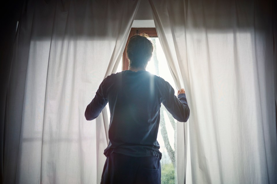 a man is looking out of a window with white curtains