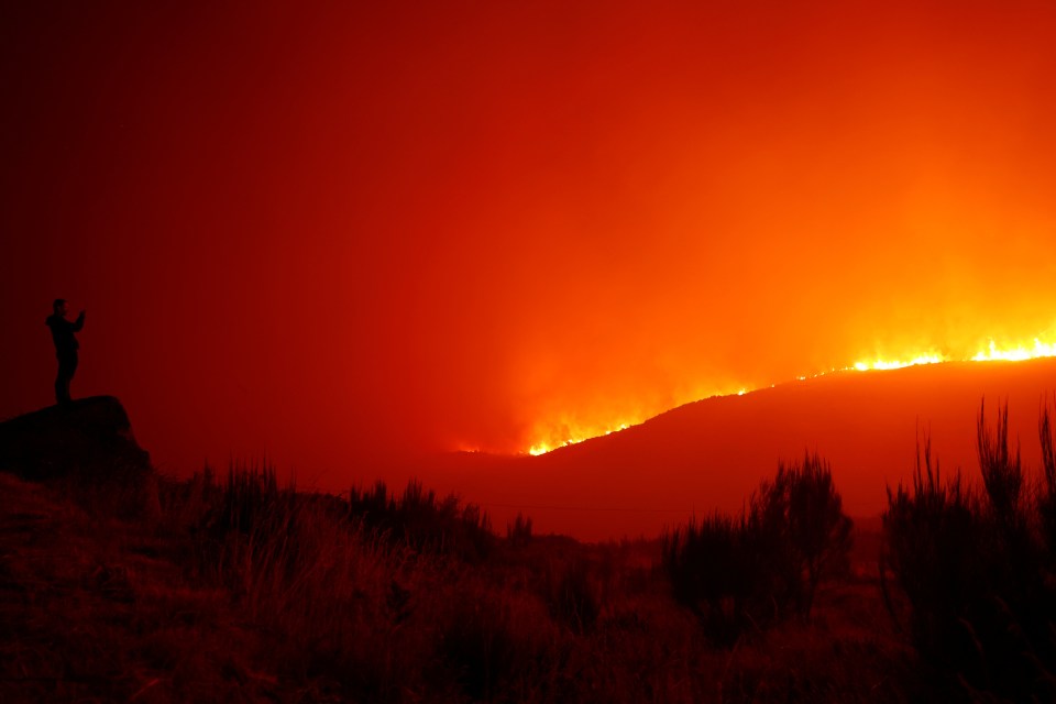 a person standing on a hill looking at a fire