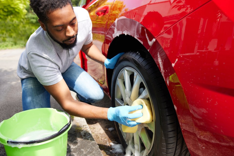 a man washing a red car with a yellow sponge