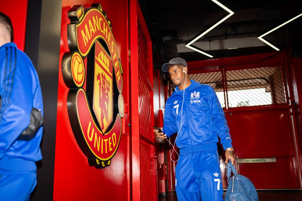 a man wearing a blue adidas tracksuit stands in front of a manchester united sign