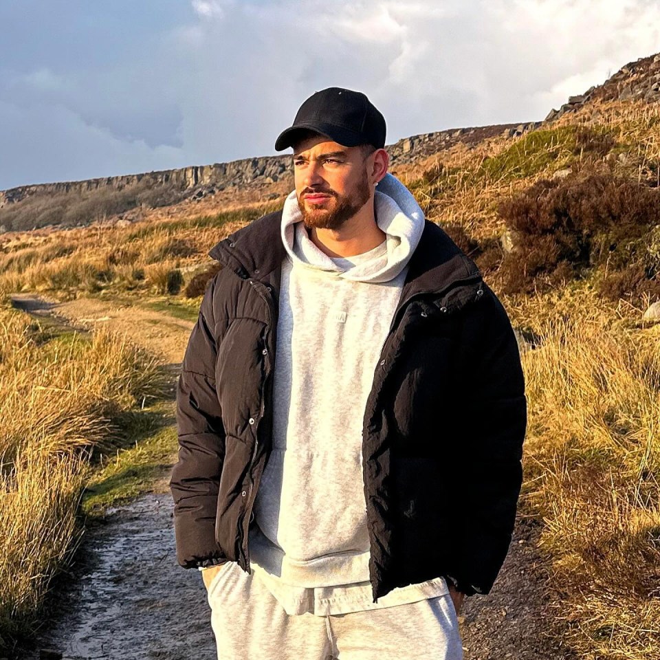 a man wearing a black jacket and a hat stands in a field