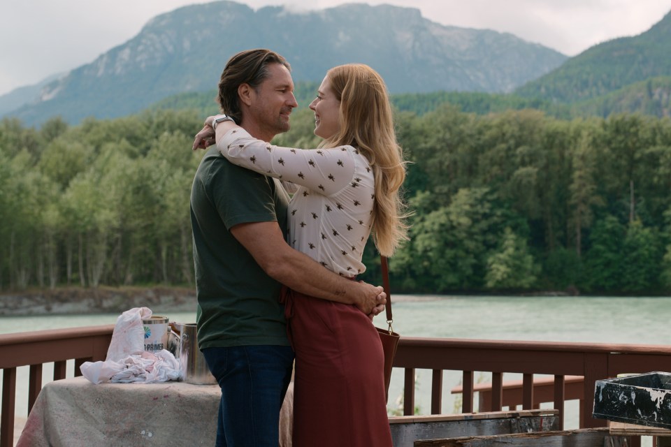 a man and woman hugging on a deck with mountains in the background