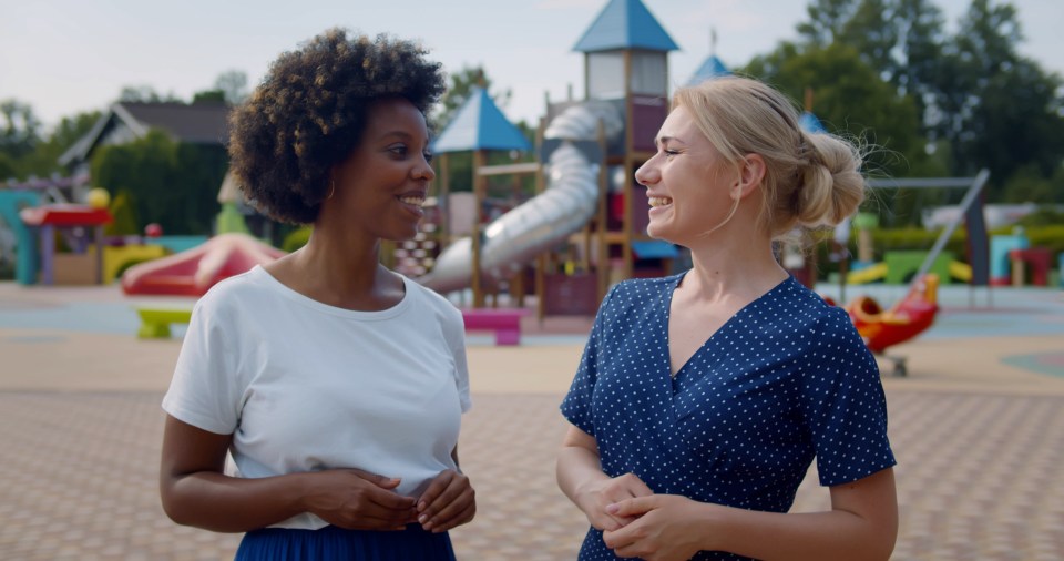 two women standing next to each other in front of a playground