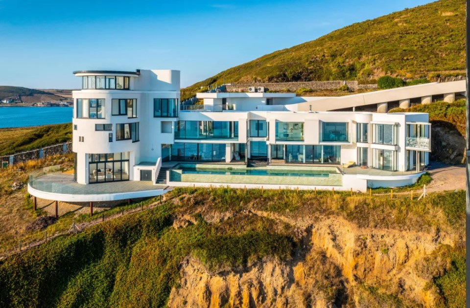 a large white house sits on top of a hill overlooking the ocean