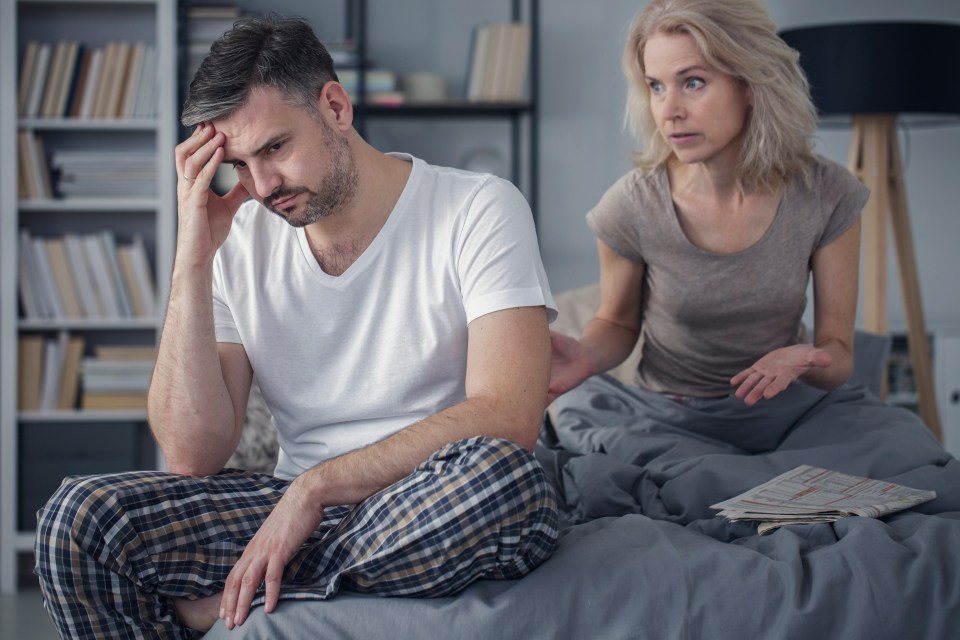 a man sits on a bed while a woman talks to him