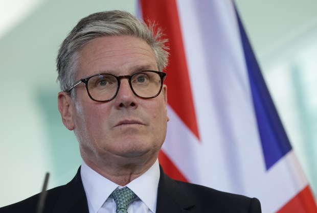 a man wearing glasses and a suit stands in front of a flag