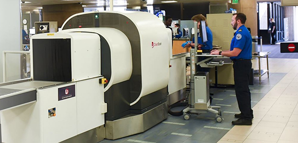 a man in a blue uniform stands in front of a machine that says ' x-ray ' on it