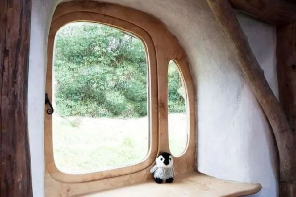 a stuffed penguin is sitting on a window sill in a wooden house .