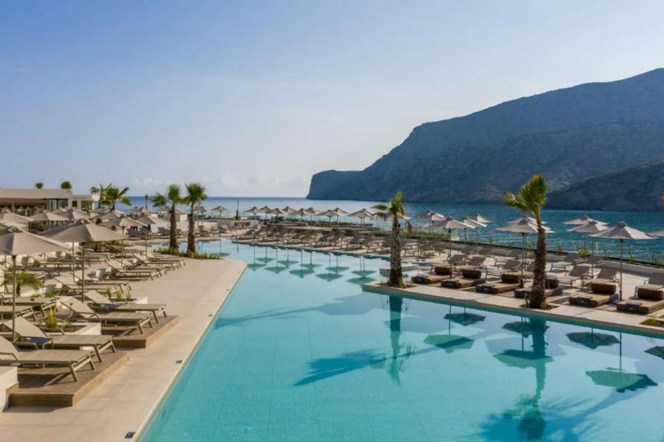 a large swimming pool surrounded by chairs and umbrellas with a mountain in the background