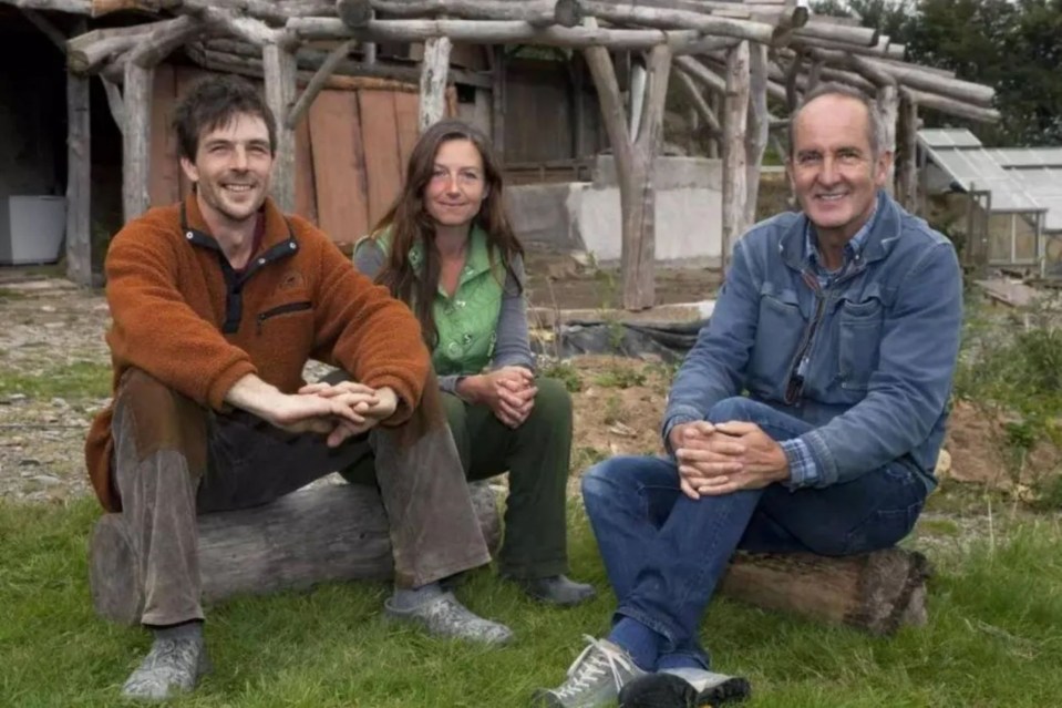 a man and two women sit on a log in the grass