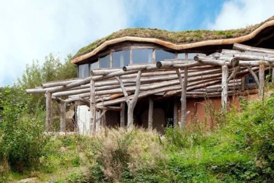 a wooden house with a green roof is sitting on top of a grassy hill .