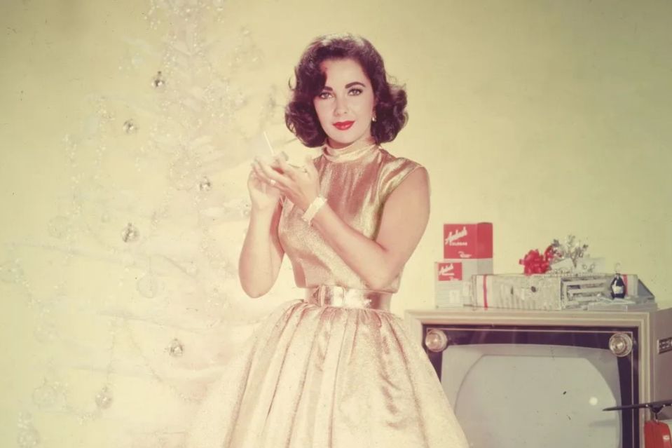 a woman in a gold dress stands in front of a christmas tree