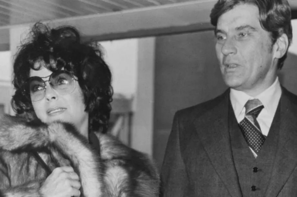 a man in a suit and tie stands next to a woman in a fur coat