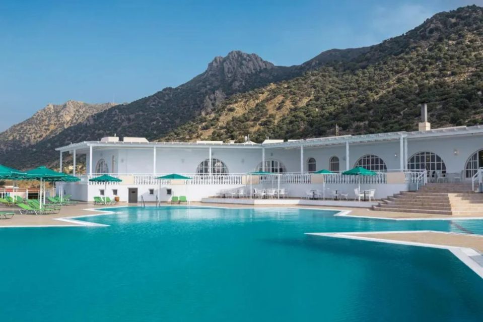 a large swimming pool in front of a hotel with mountains in the background