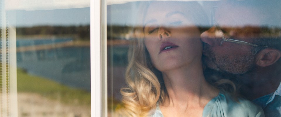 a man kisses a woman on the neck behind a window