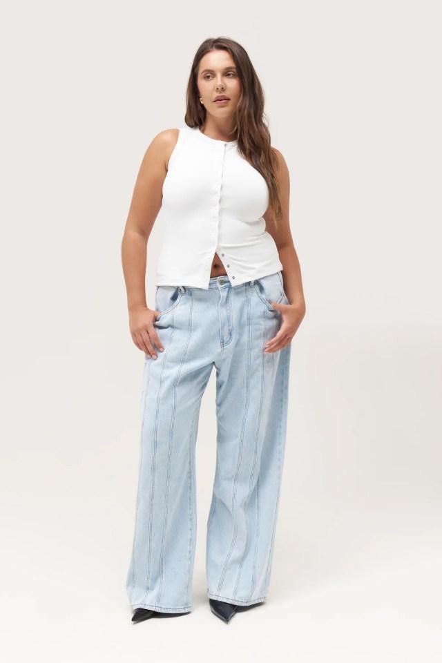 a woman wearing a white tank top and wide leg jeans