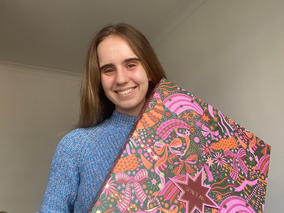 a woman in a blue sweater is holding a space nk box