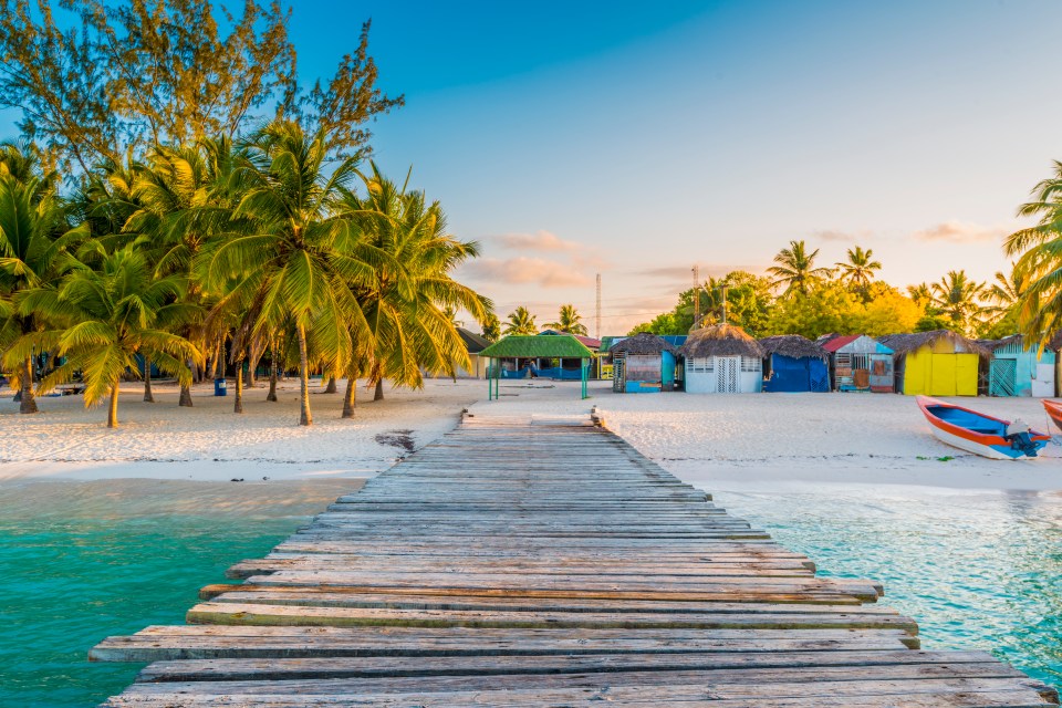 a wooden dock leads to a tropical beach with colorful huts