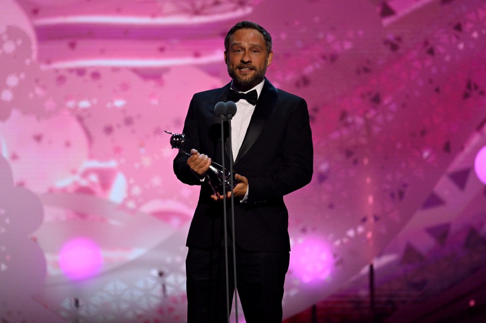 a man in a tuxedo holds a trophy in front of a microphone