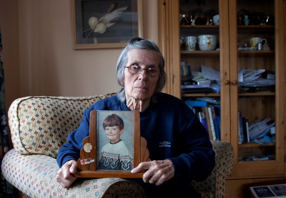 an elderly woman holding a framed picture of a young boy wearing a blue umbro sweatshirt