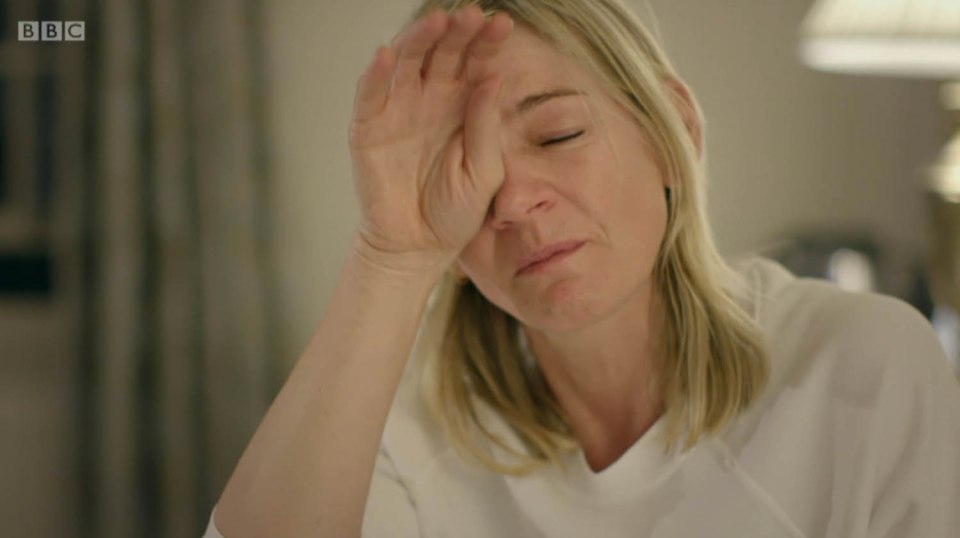 a woman holds her hand to her forehead in front of a bbc logo