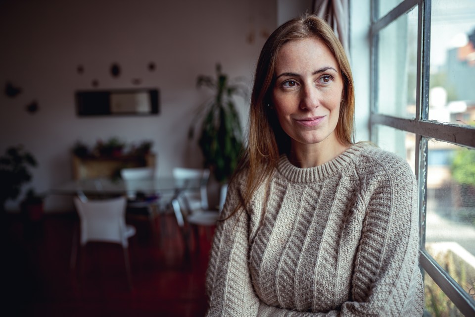 a woman in a sweater looks out a window