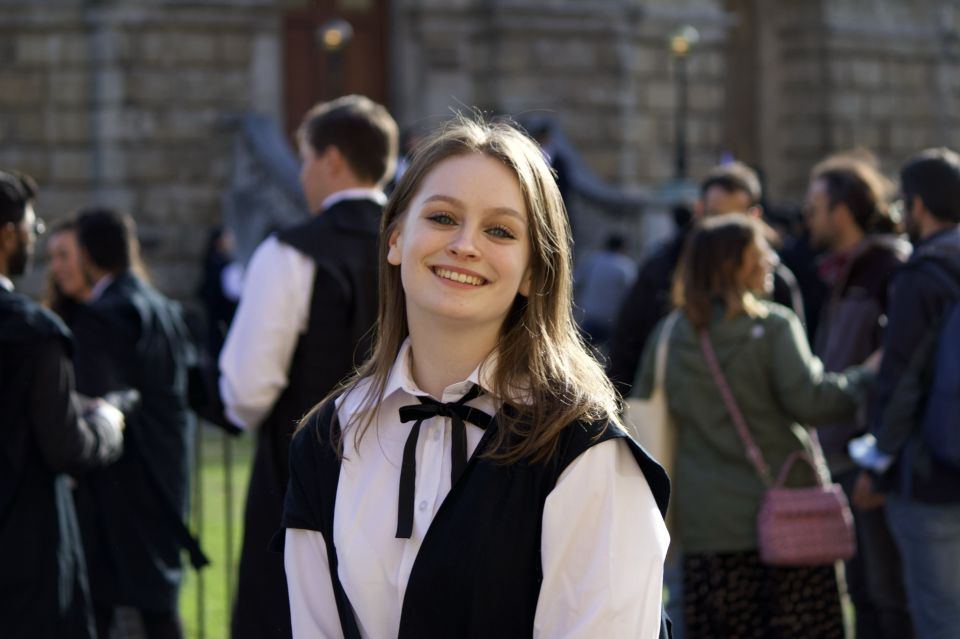 a woman in a white shirt and black vest smiles in front of a crowd