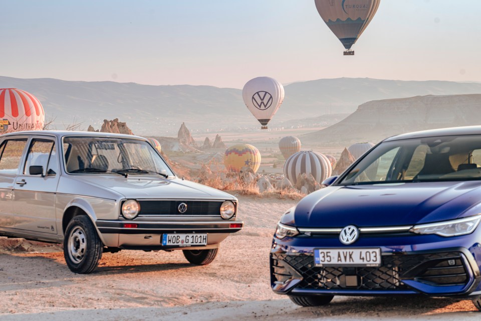 two volkswagen cars are parked next to each other with hot air balloons in the background