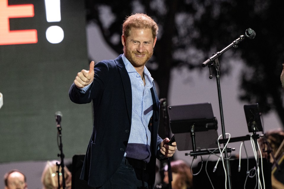 prince harry giving a thumbs up in front of a microphone