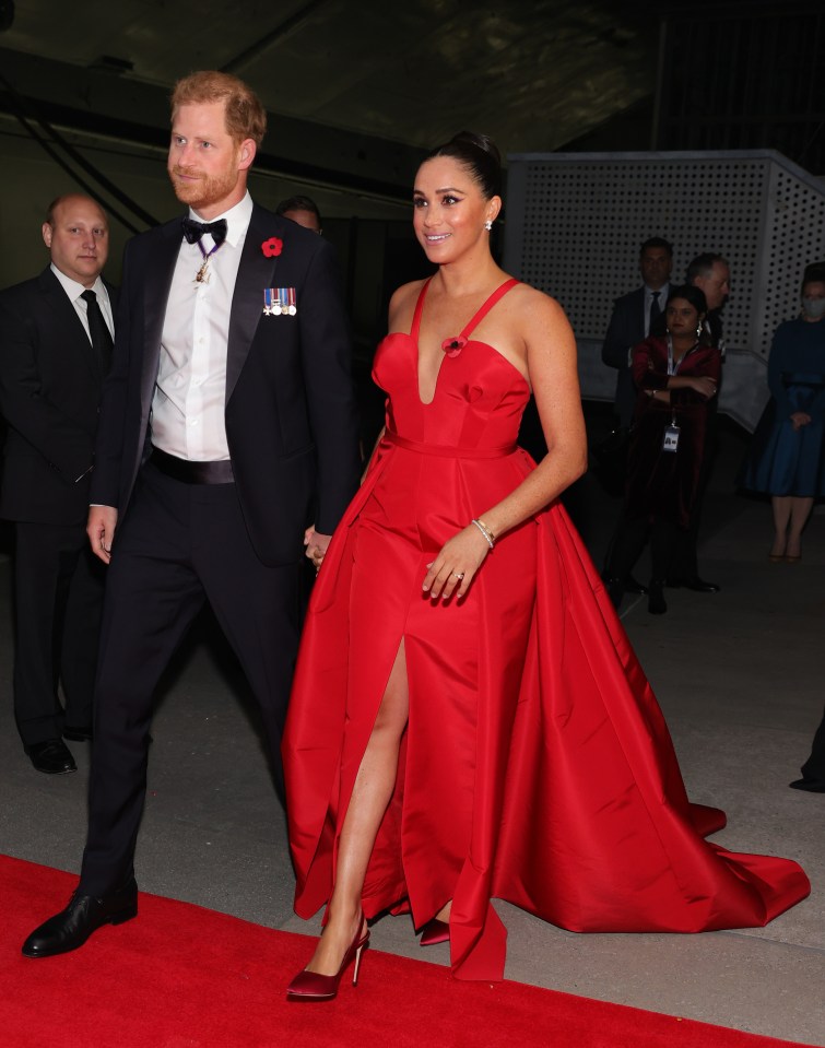 a man in a tuxedo and a woman in a red dress walk on a red carpet