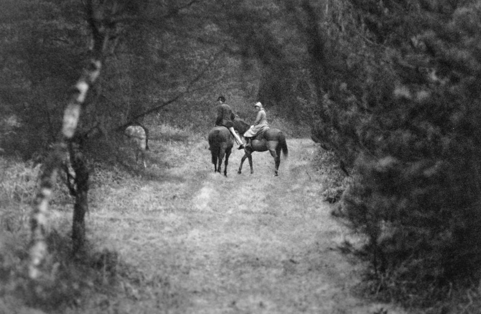 a black and white photo of people riding horses