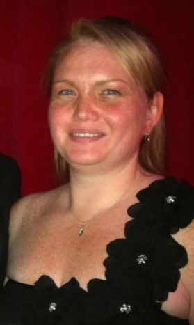 a woman in a black dress with flowers on the shoulder is smiling for the camera .