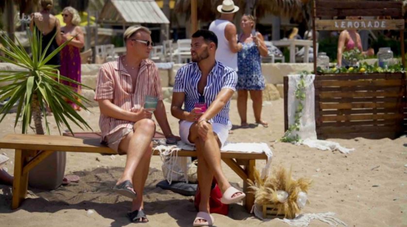 two men sit on a bench in front of a lemonade stand