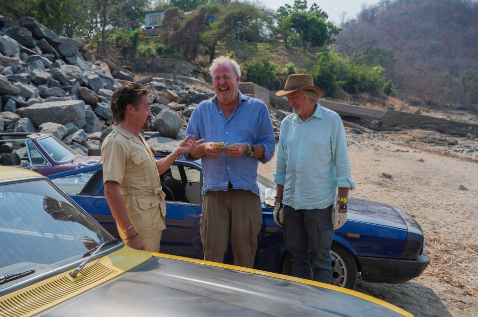 three men are standing next to a blue car and laughing